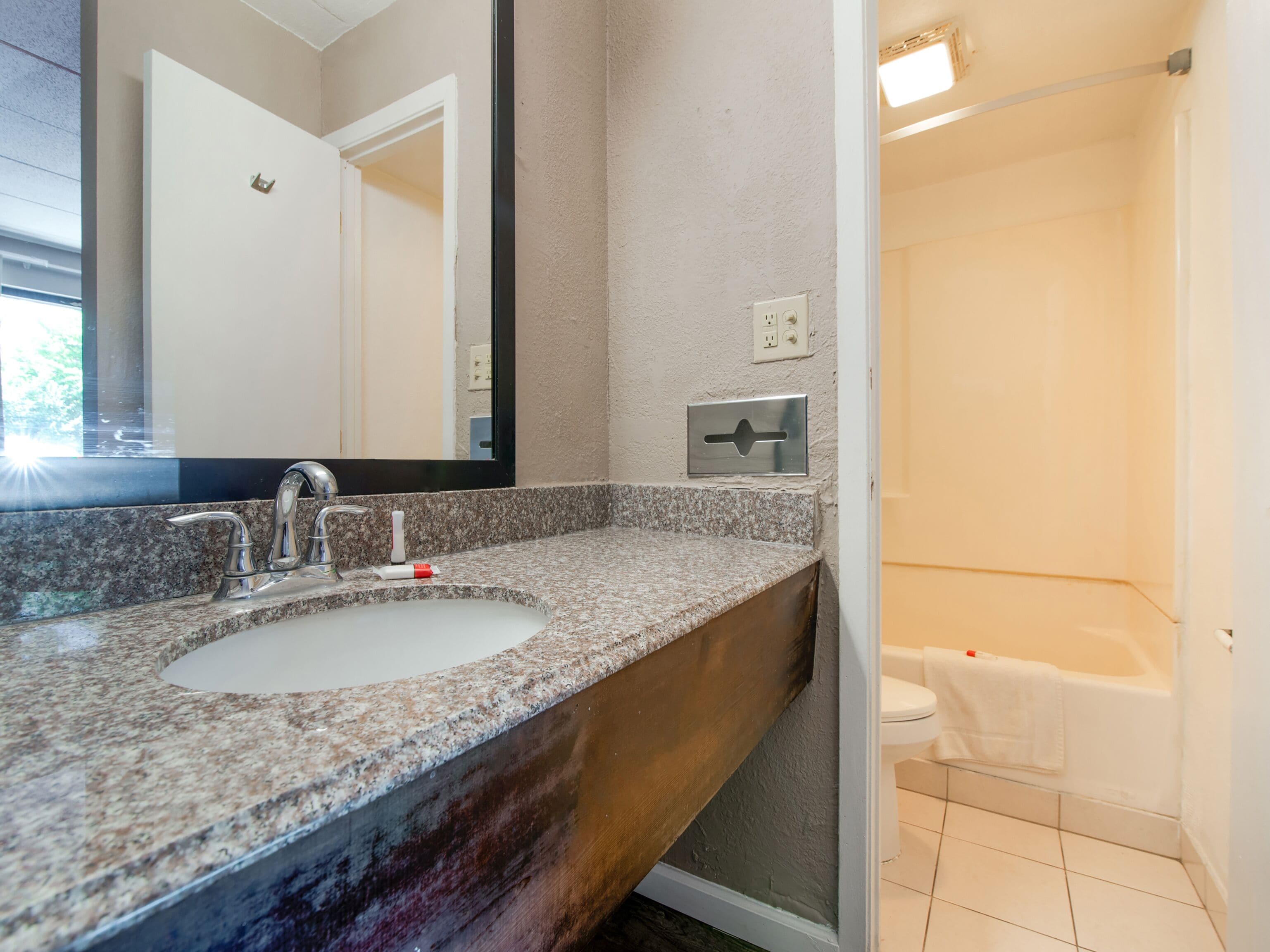 A bathroom with a granite countertop sink, a mirror, and a shower.