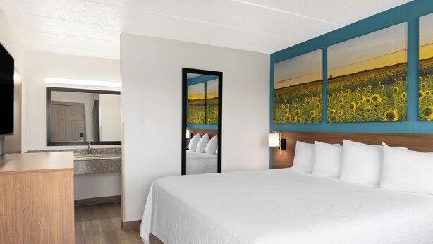 Une chambre d’hôtel avec un grand lit, un bureau en bois, un miroir et un mur orné d’un tableau représentant des tournesols.