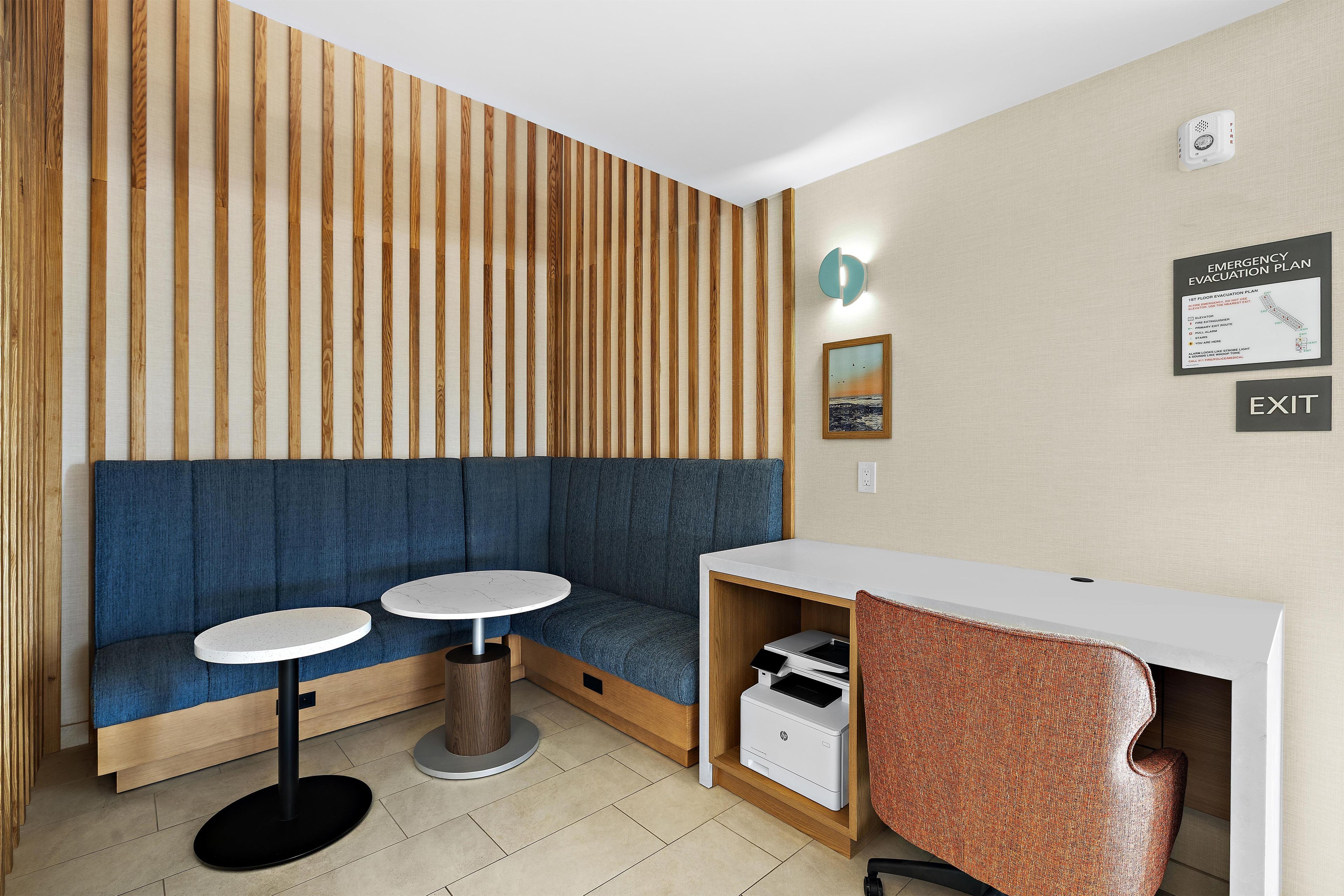 Una habitación moderna con pared de listones de madera, un sofá azul, dos mesas redondas, un escritorio blanco y una impresora HP.