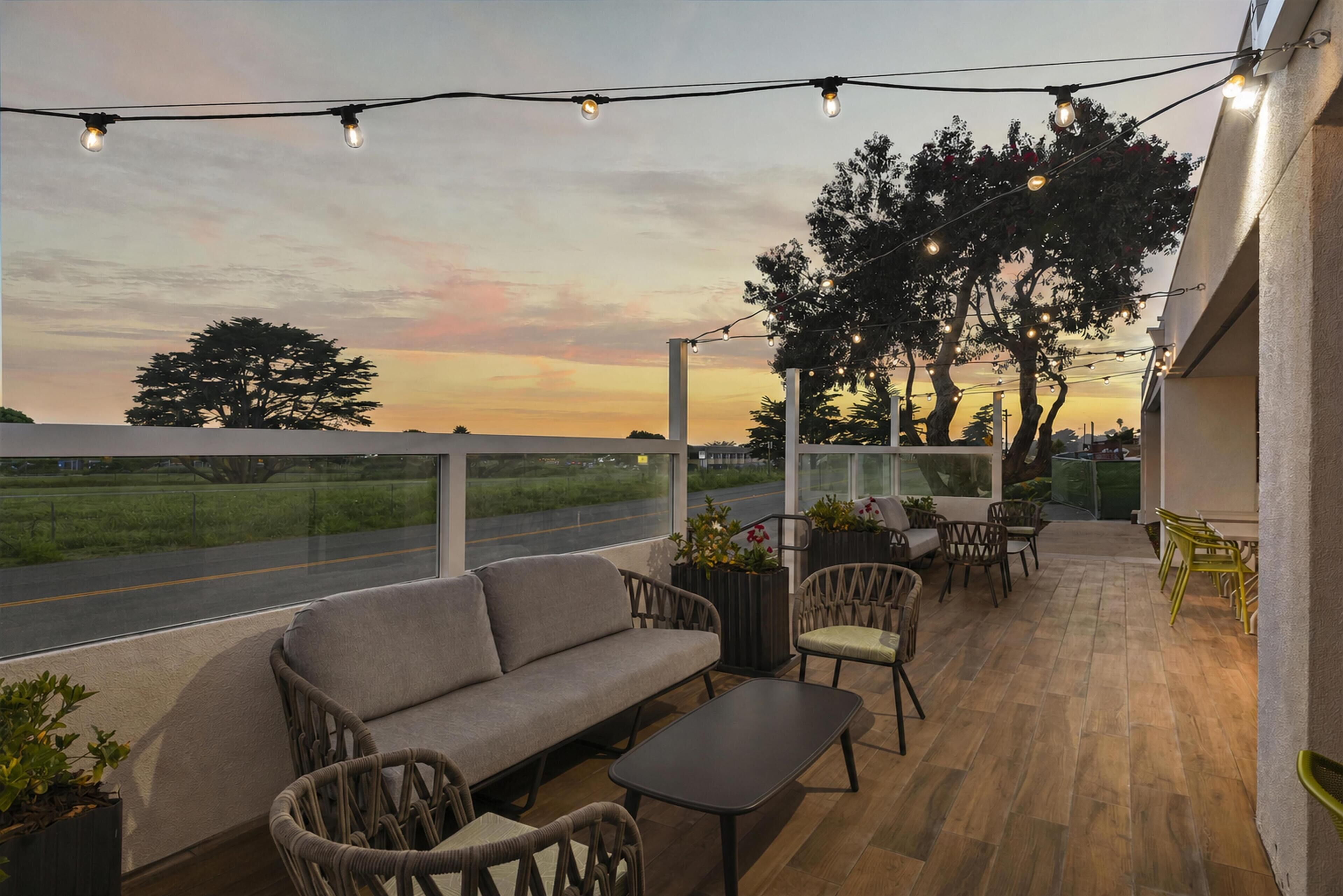 Un espacio de estar al aire libre con sofá, sillas y una mesa, con vistas a una calle y árboles.
