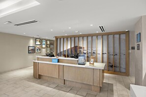 A hotel reception desk with a wooden finish, a digital display, and framed artwork on the wall. - Hampton Inn San Simeon Cambria (San Simeon)