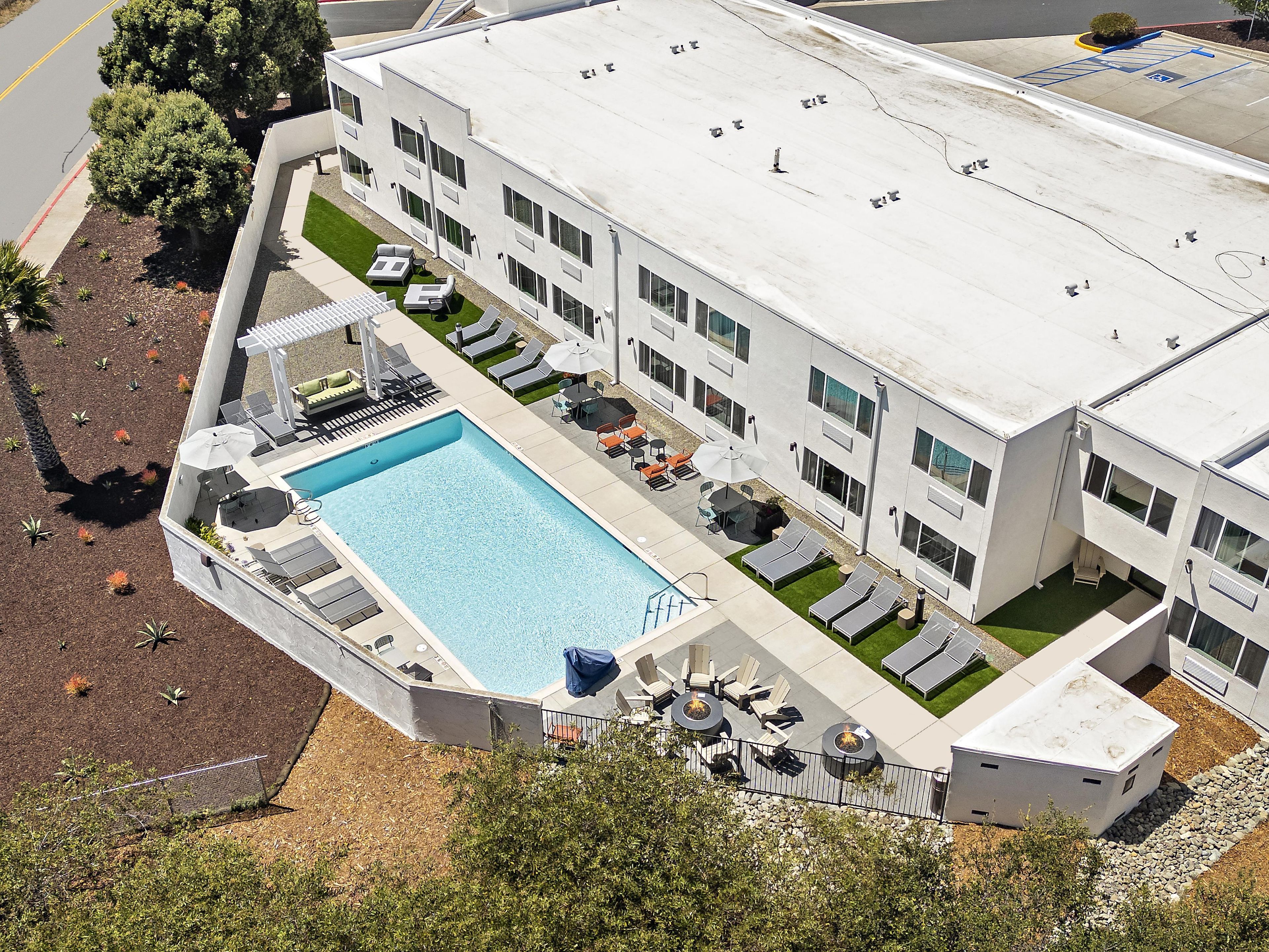 A modern building with a rooftop pool, sun loungers, and a landscaped patio area.