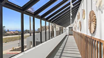 A corridor with large windows, a wooden floor, and decorative wall panels.