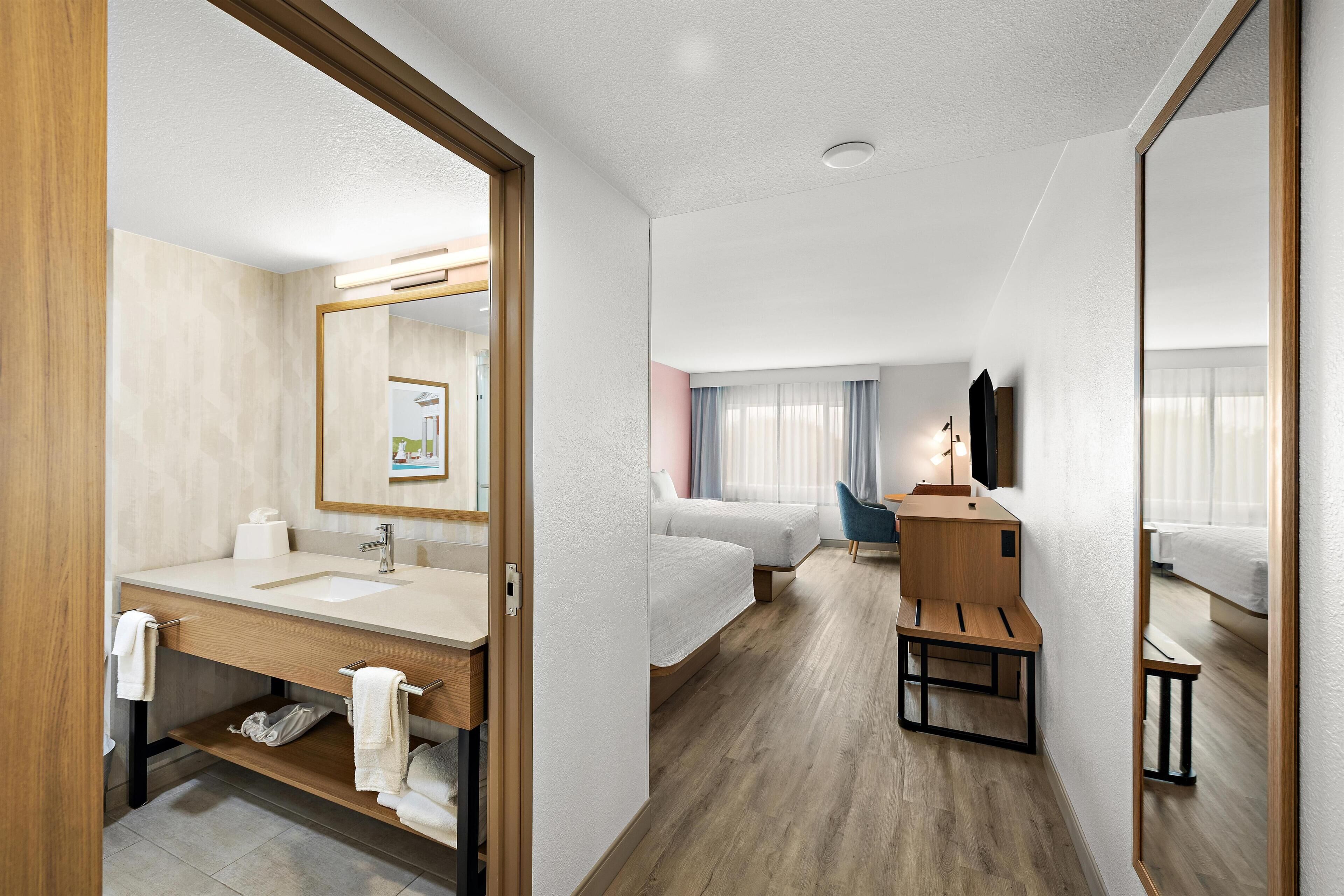 A hotel room with a bathroom, a bed, a desk, and a mirror.
