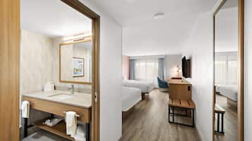 A hotel room with a bathroom, a bed, a desk, and a mirror.