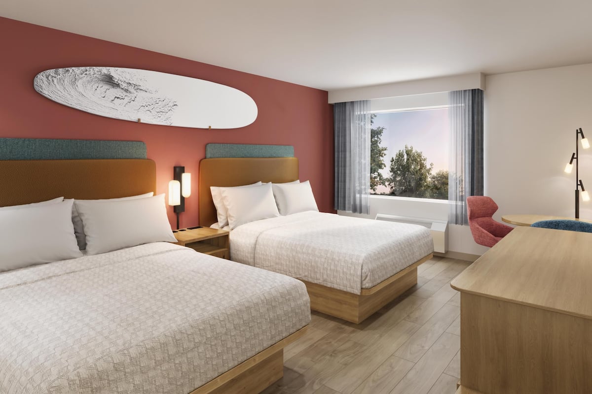 A hotel room with two beds, a large window with a view, a desk, and a chair.