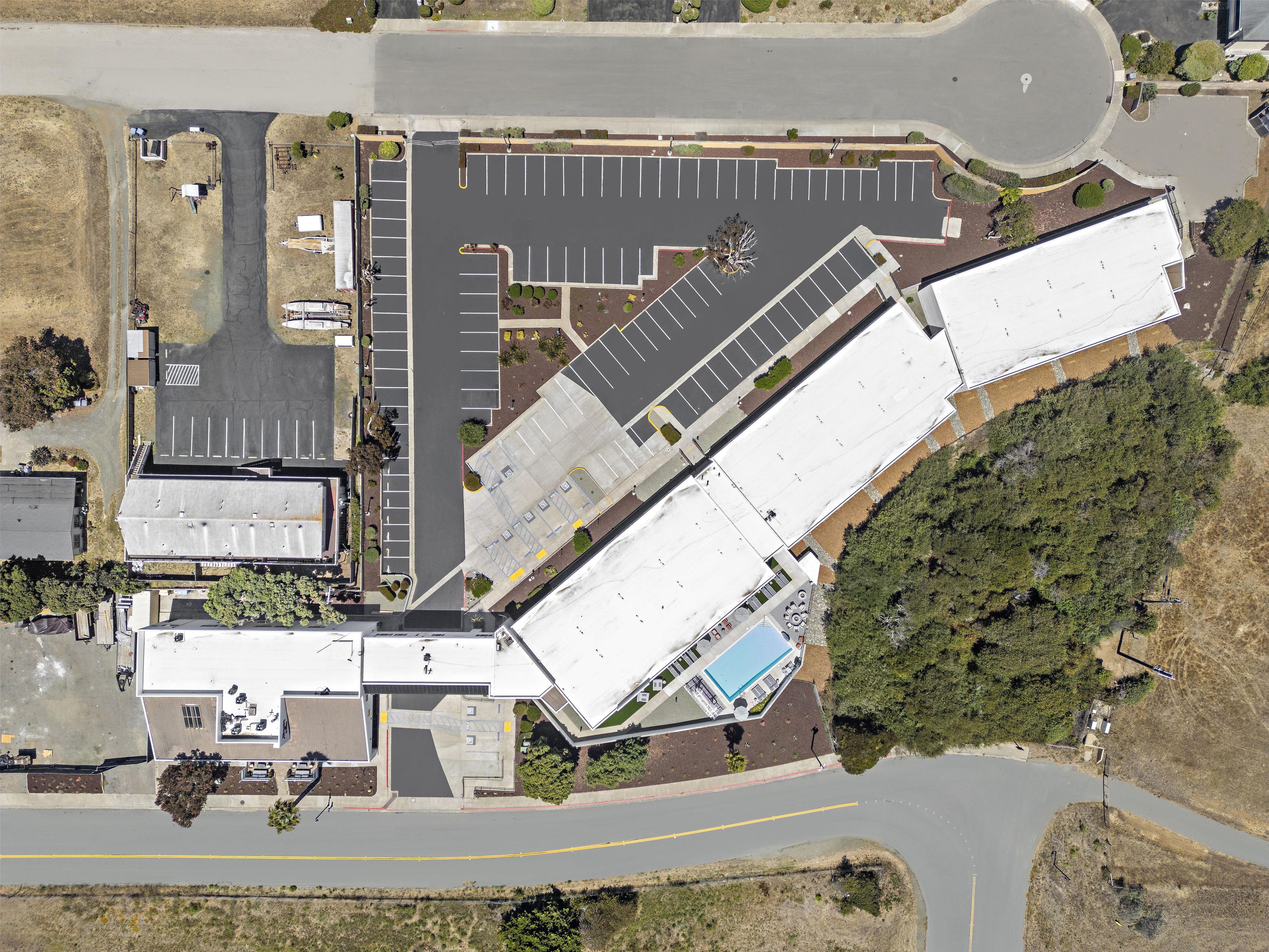 An aerial view of a building with a large parking lot, a swimming pool, and a landscaped area.