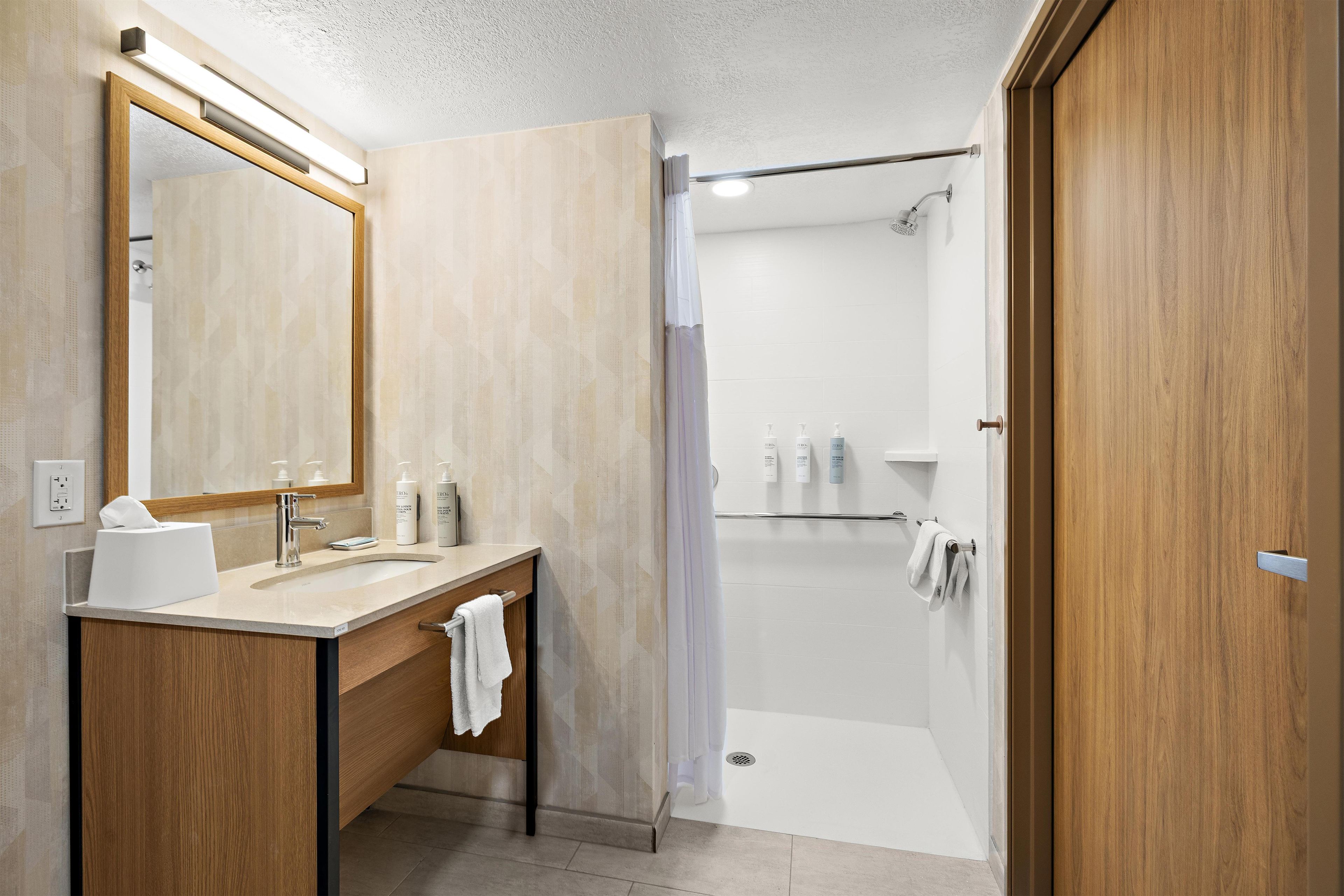 A modern bathroom with a wooden vanity, a large mirror, and a shower area.