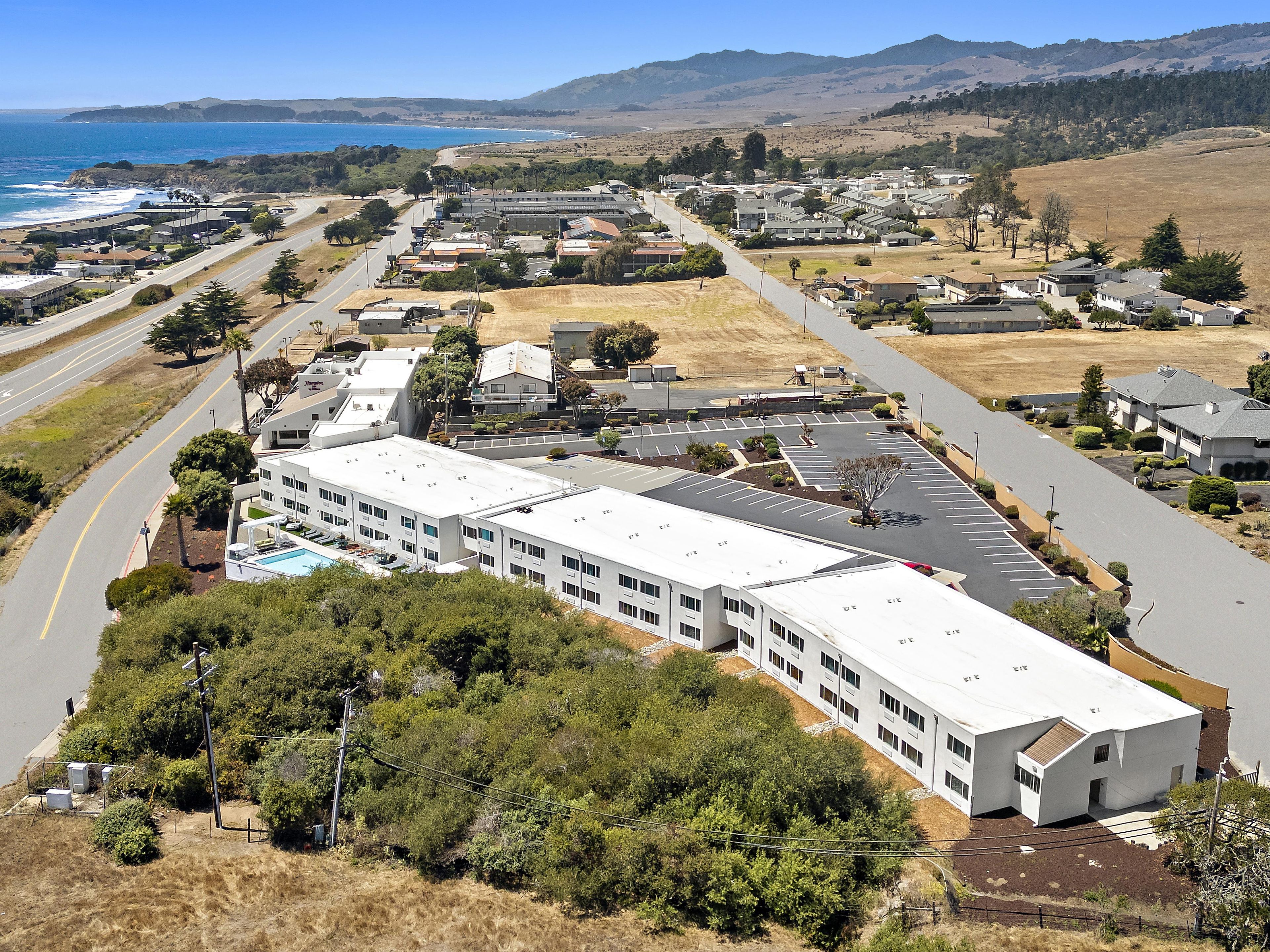 A large building with multiple parking spaces and a road leading to the ocean.