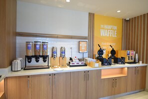 Ein Frühstücksbuffet mit Kaffeeautomaten, Waffelgeräten und einem Schild mit der Aufschrift 'The Hampton Waffle'.