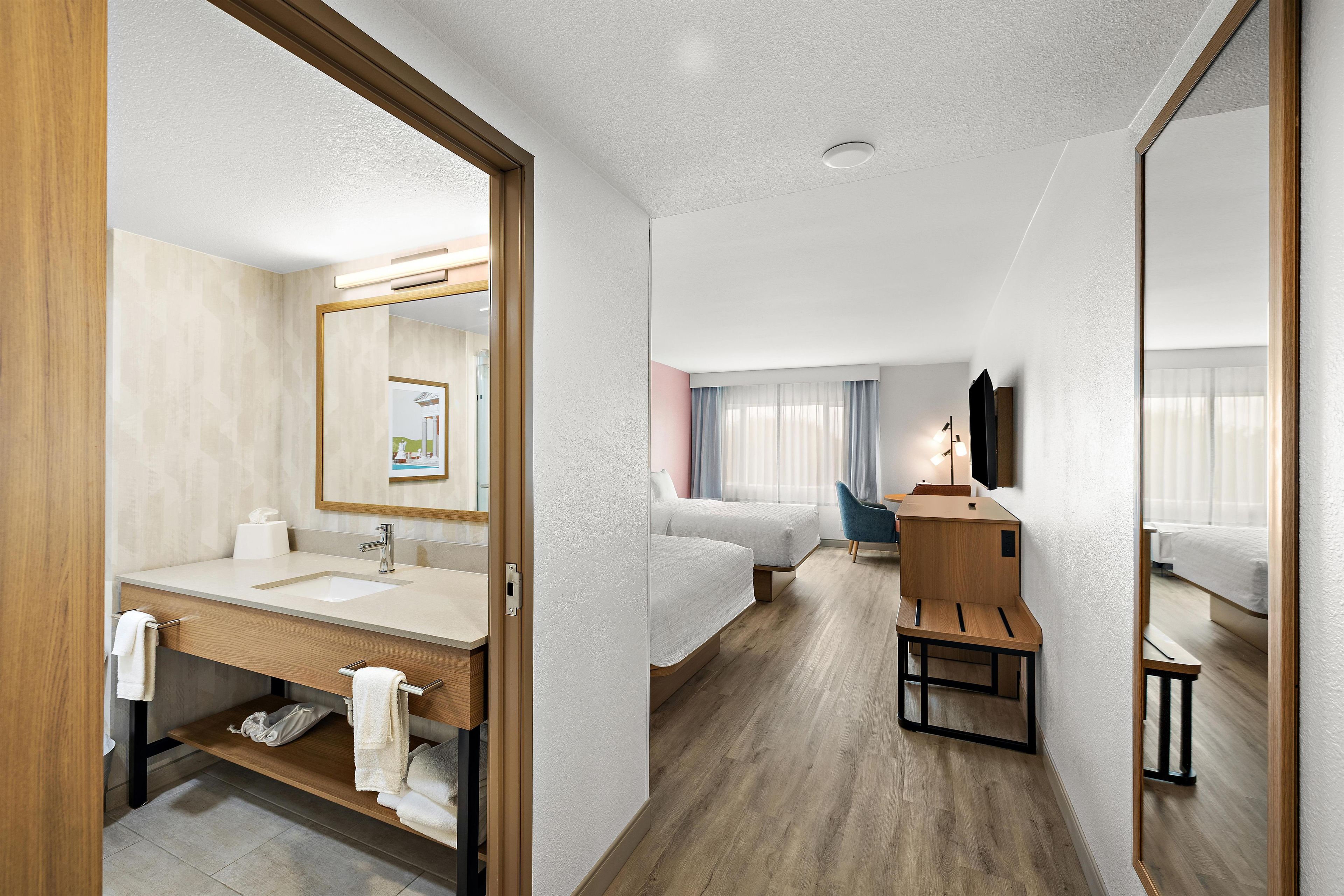 A hotel room with a bathroom, a bed, a desk, and a mirror.