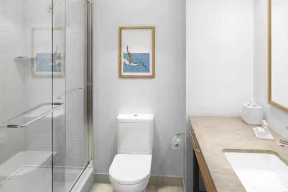 A modern bathroom with a glass shower enclosure, a toilet, a sink, and a framed picture on the wall.