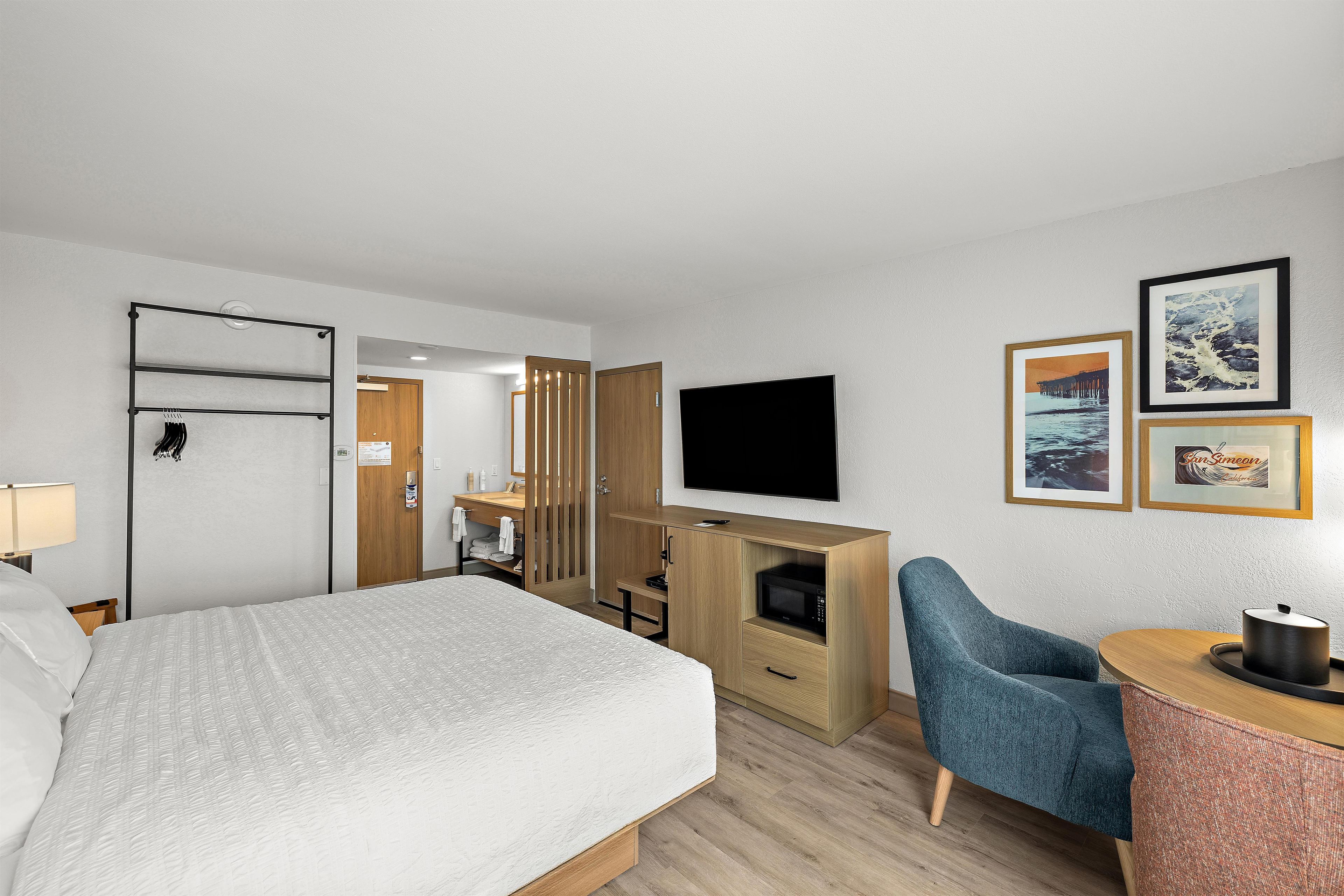 A hotel room with a bed, a desk with a chair, a television, and artwork on the wall.