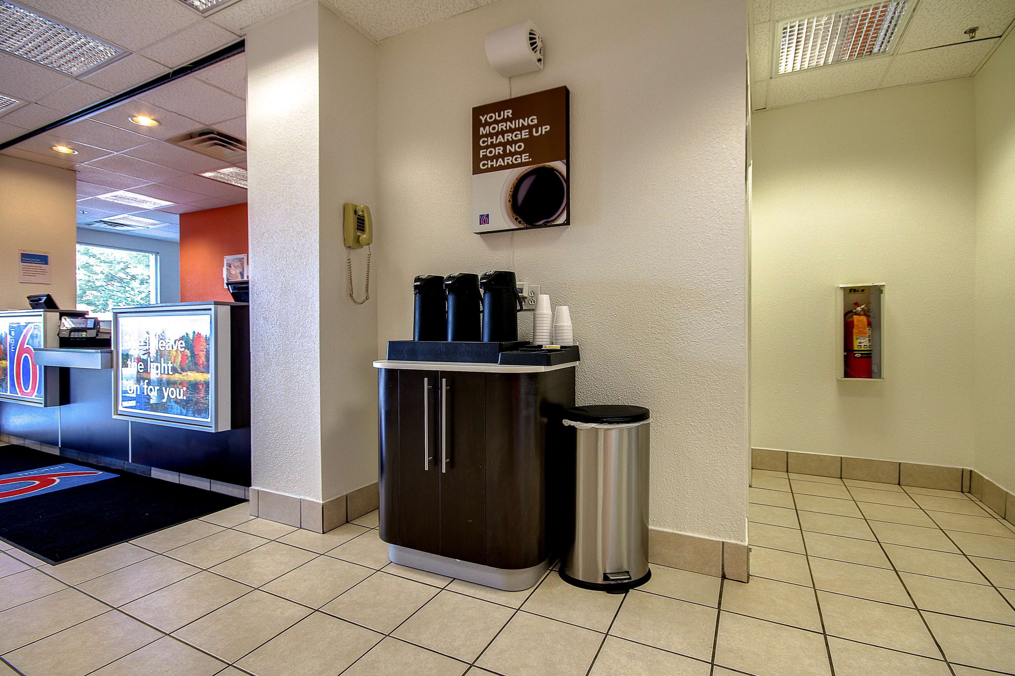 Un espace d’accueil d’hôtel comprenant un coin café, une poubelle et un panneau placé au-dessus du coin café.