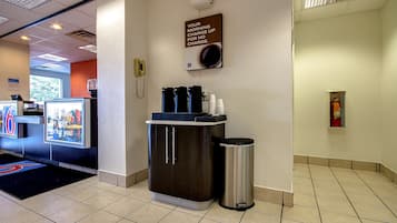 Uma área de recepção de hotel com um espaço para café, uma lixeira e uma placa acima do espaço para café.