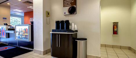 Un espace d’accueil d’hôtel comprenant un coin café, une poubelle et un panneau placé au-dessus du coin café.