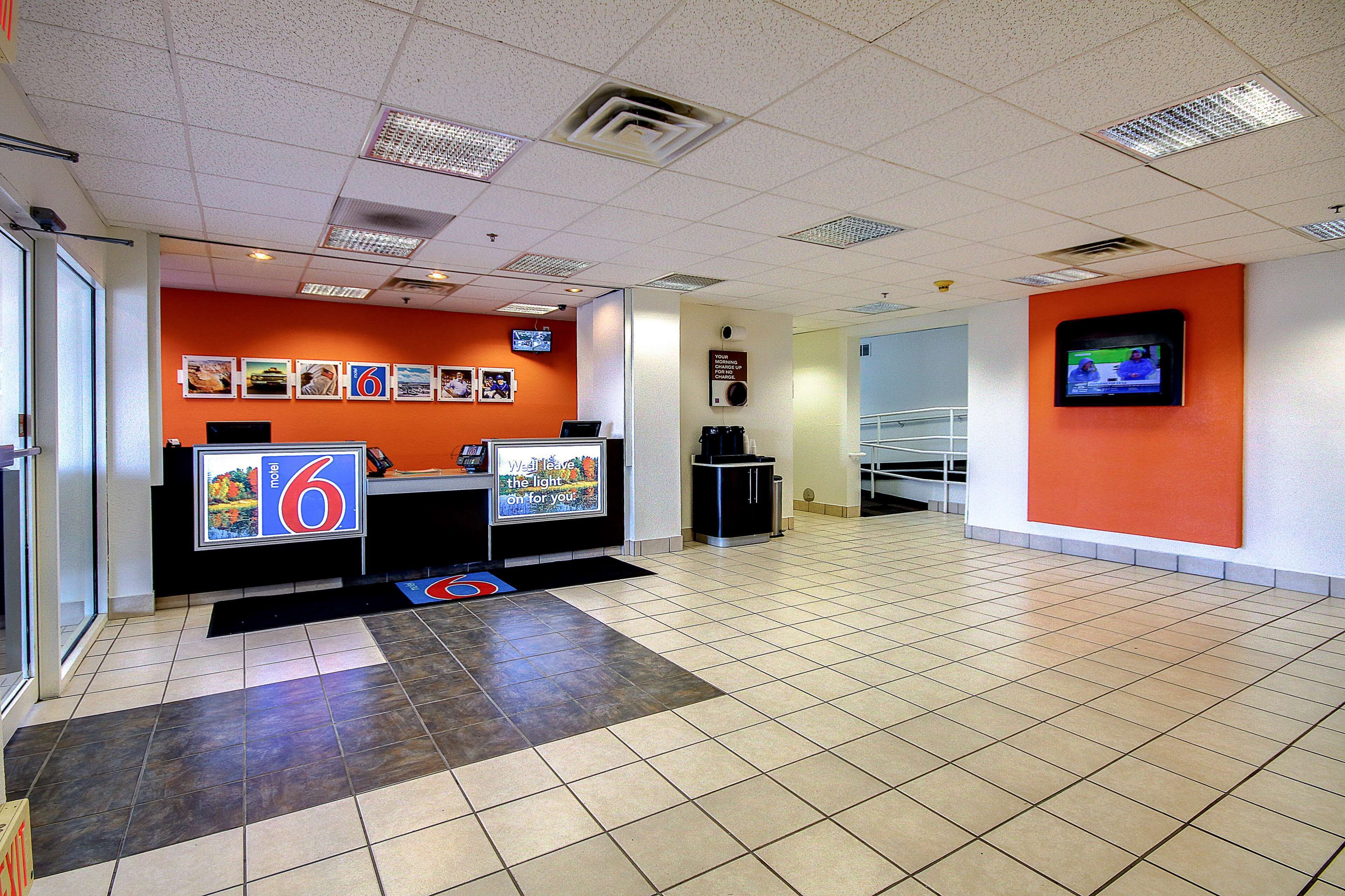 A spacious lobby with a reception desk, a large screen, and a tiled floor.