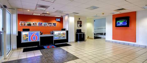 A spacious lobby with a reception desk, a large screen, and a tiled floor.