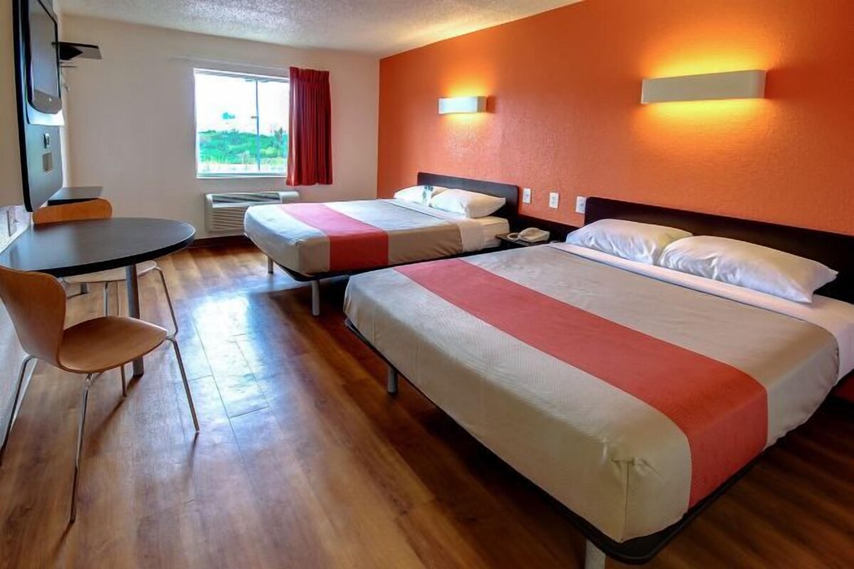 A hotel room with two beds, a desk, a chair, and a window with curtains.