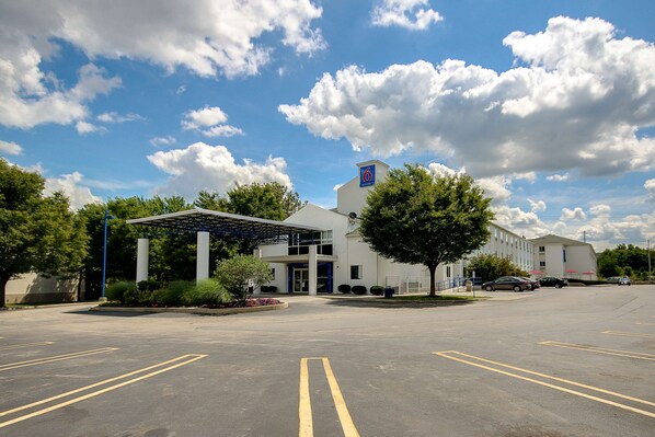A hotel with a covered entrance, a parking lot, and a clear blue sky with clouds. - Motel 6 King Of Prussia, PA - Philadelphia (Wayne)