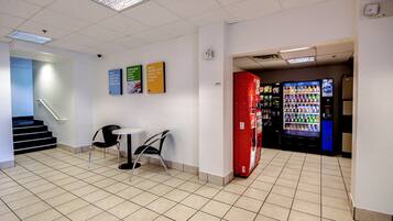 A lobby with a vending machine, a table with chairs, and a staircase.