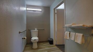 Un baño con inodoro, barras de apoyo, un perchero y un cubo de basura.