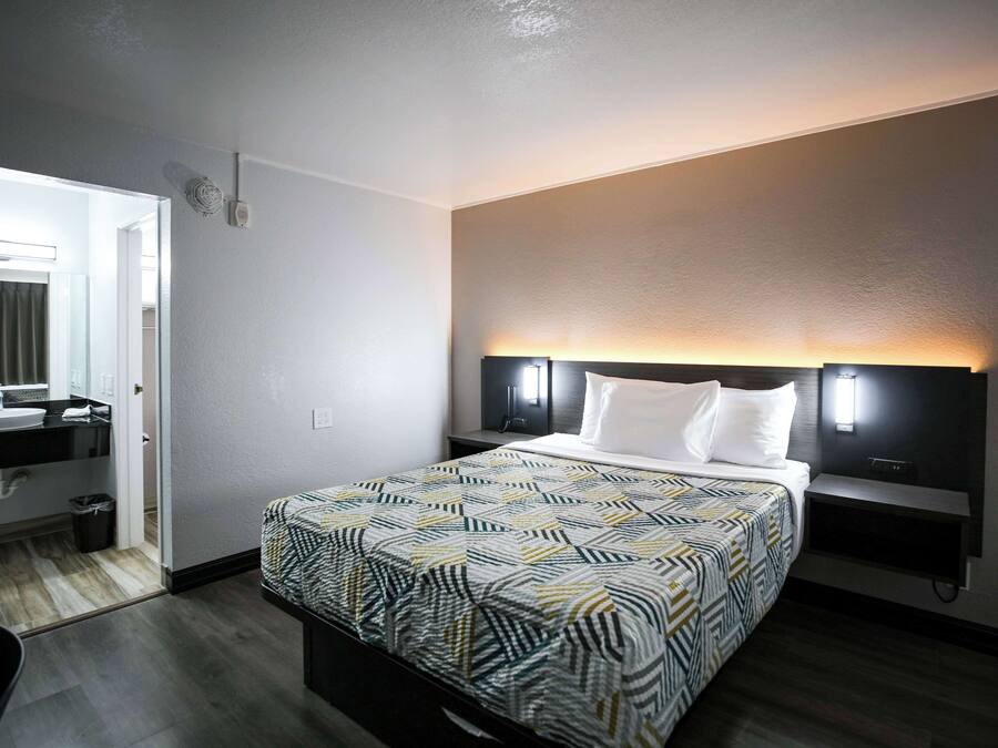 Une chambre d’hôtel comprenant un lit, des tables de chevet, une commode, un miroir, un lavabo et une poubelle.