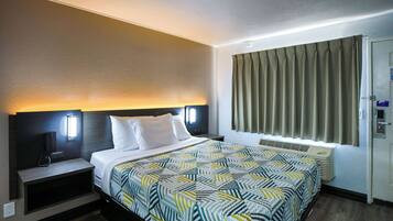 Habitación de hotel con cama, mesitas de noche, televisor montado en la pared, ventana con cortinas y una puerta.