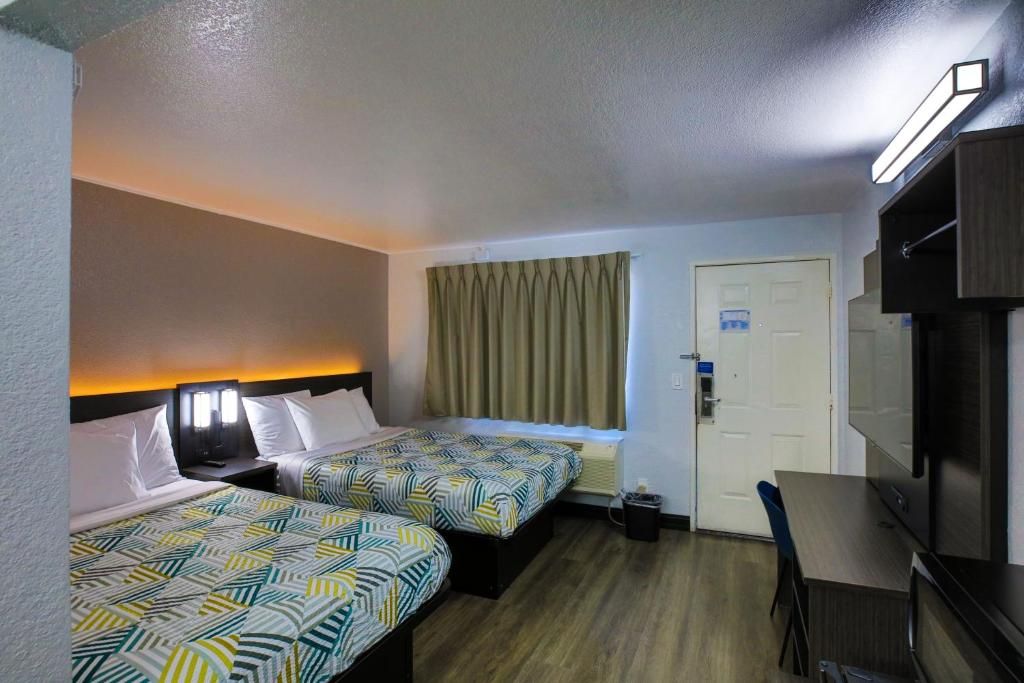 A hotel room with two beds, a desk, a television, and a door.