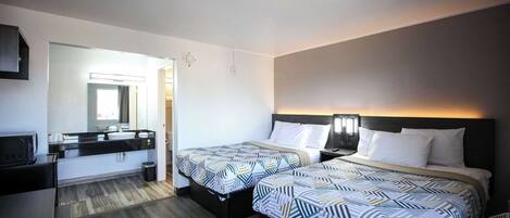 Una habitación de hotel con dos camas, un escritorio, un espejo y un baño.