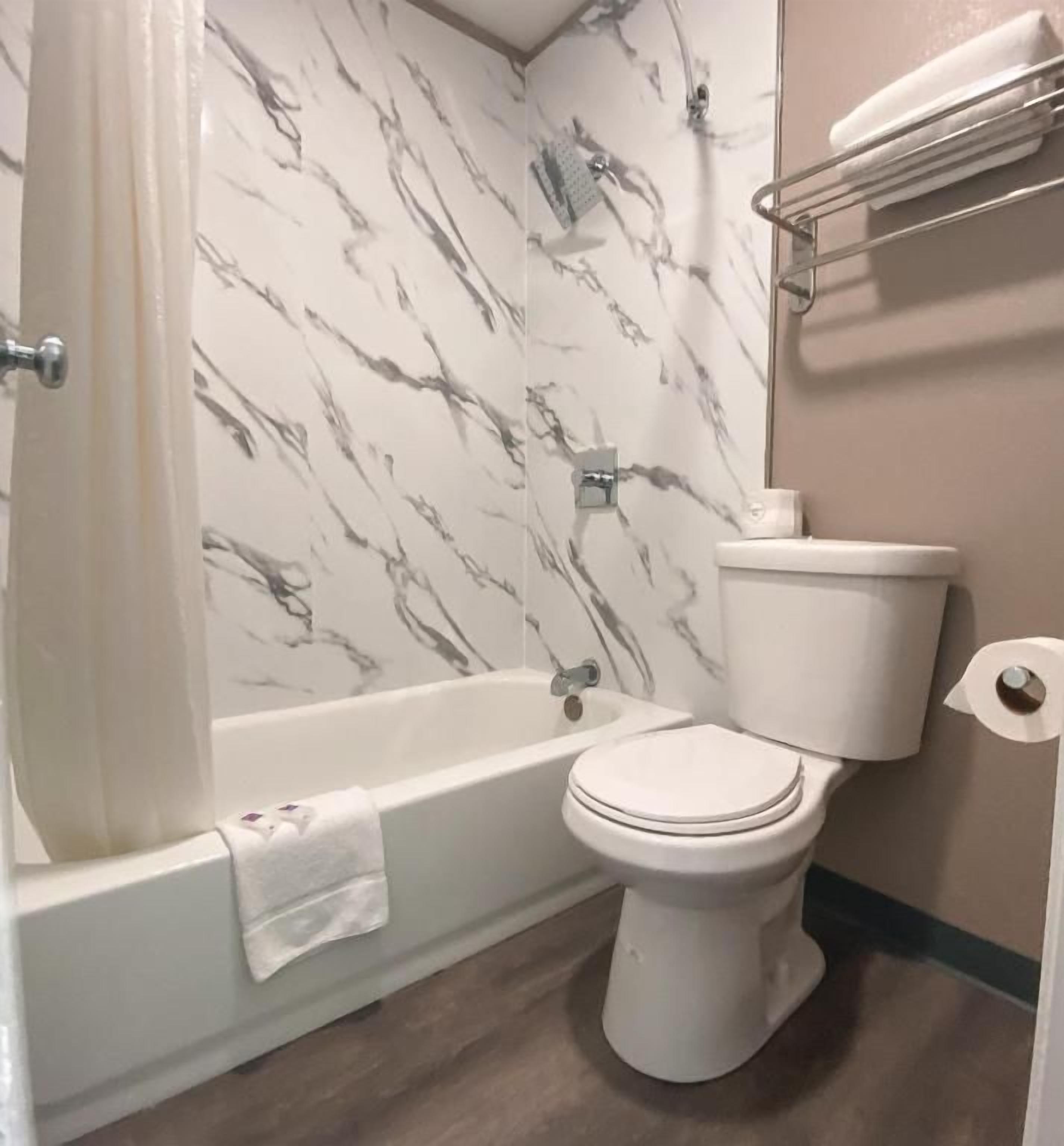 A bathroom with a bathtub, toilet, and marble-patterned walls.