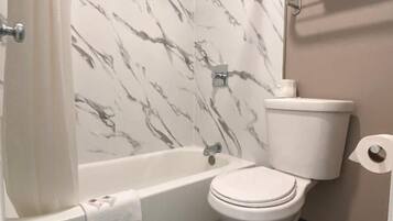 A bathroom with a bathtub, toilet, and marble-patterned walls.