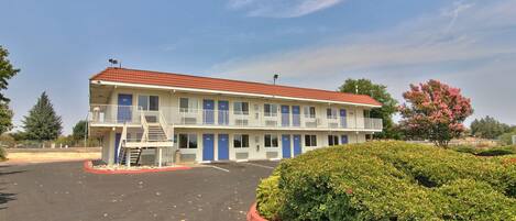 A motel with a red roof, multiple blue doors, and a parking lot.