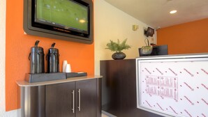 Ein Empfangsbereich mit Wandfernseher, der ein Sportspiel zeigt, einer Rezeption, einem Telefon und einer Pflanze.