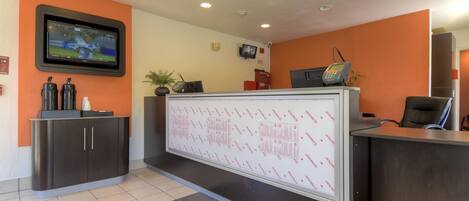 Zona de recepción con televisor de pantalla plana, un tablón informativo grande, teléfono y escritorio.