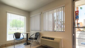 Ein Zimmer mit zwei Fenstern, einem Tisch, zwei Stühlen und einer Wand-Klimaanlage.