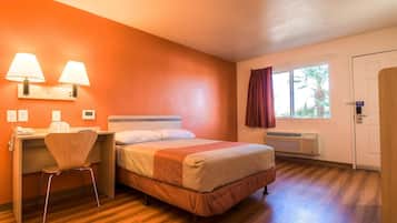 Una habitación de hotel con cama, escritorio, silla y ventana con cortinas.