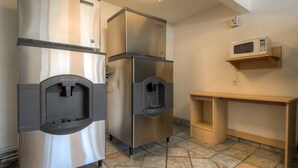 Eine Küchenzeile mit zwei Edelstahl-Kühlschränken, einer auf einem Regal stehenden Mikrowelle und einem Wasserspender.