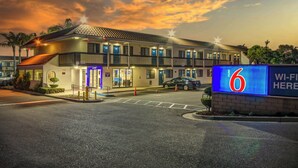 A motel with a sign indicating it is number 6, featuring a covered parking area and a clear sky.