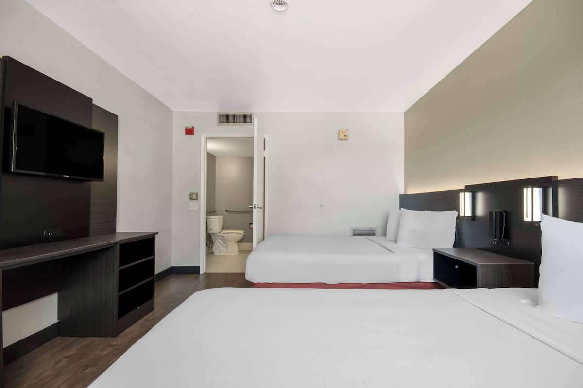 Une chambre d’hôtel équipée d’une télévision, de deux lits, d’un bureau et d’une salle de bain visible à travers une porte ouverte.
