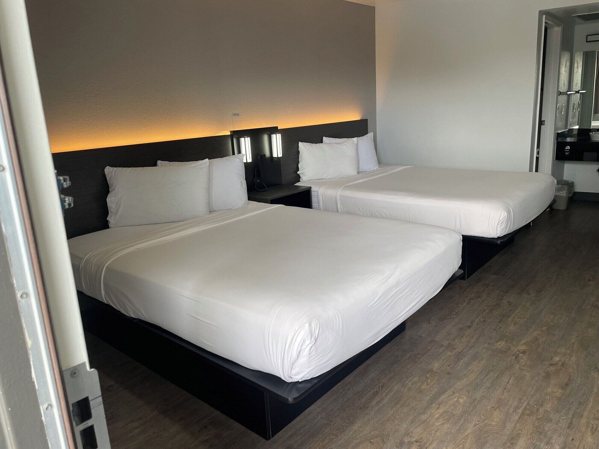 A hotel room with two beds, a dark headboard, and a small bedside table with a lamp.