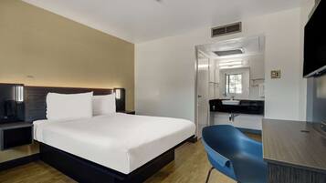Een moderne hotelkamer met een groot bed, een bureau, een blauwe stoel, en een badkamer zichtbaar door een open deur.