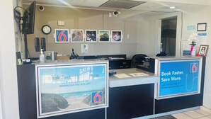 A reception desk with a digital screen displaying a beach view and promotional text for booking.