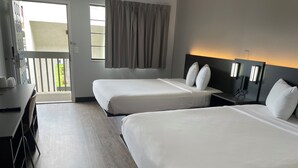 A hotel room with two beds, a desk, a chair, a nightstand, and a window with curtains.