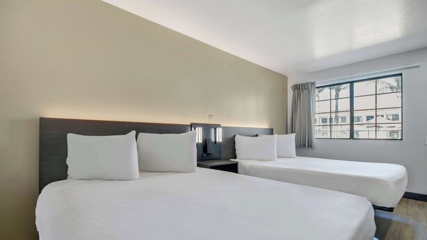 A hotel room with two beds, a nightstand, a lamp, and a window with curtains.