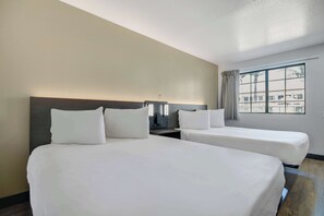Een hotelkamer met twee bedden, een nachtkastje, een lamp en een raam met gordijnen.