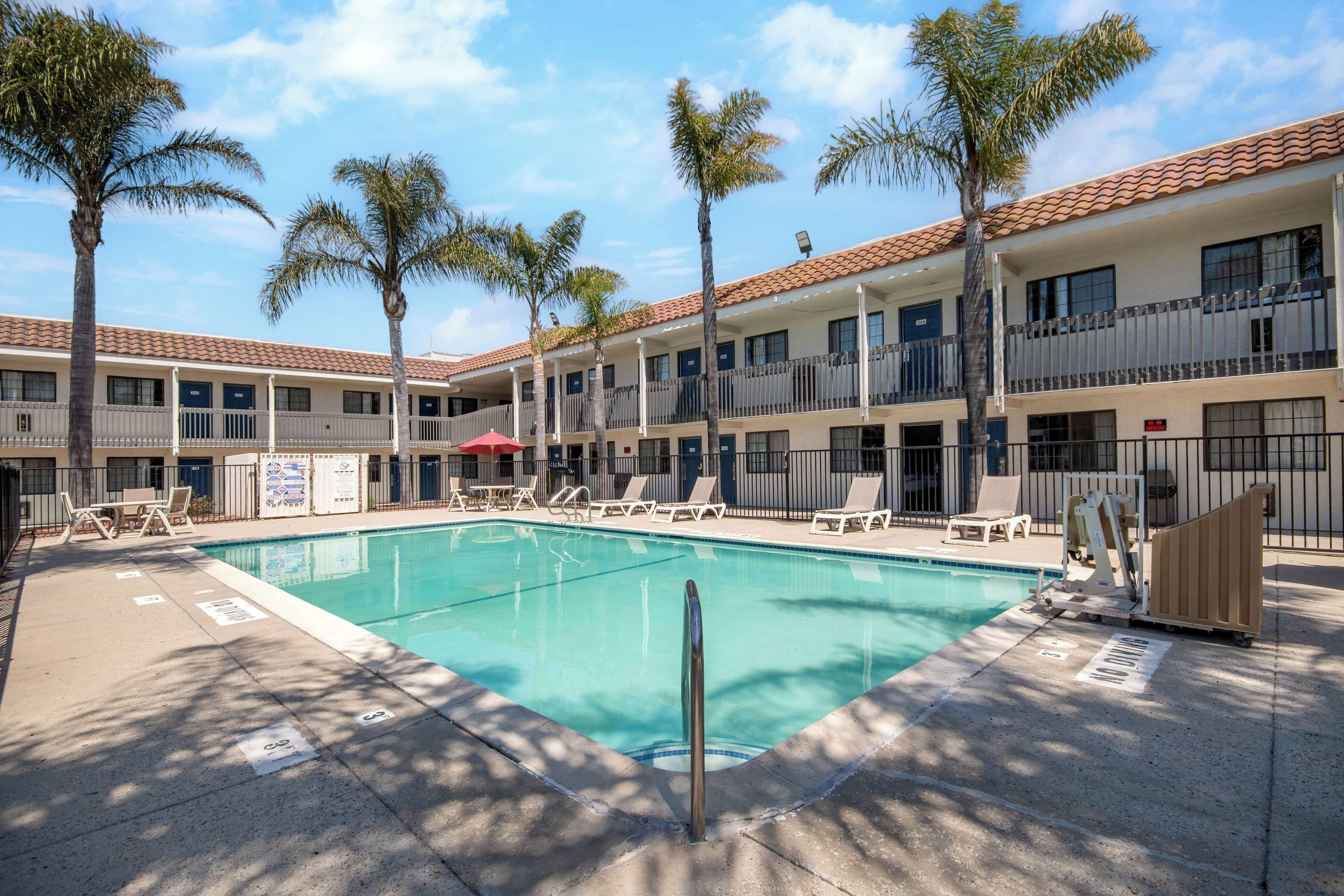 Un hotel con piscina, palmeras y un edificio de dos pisos con balcones.