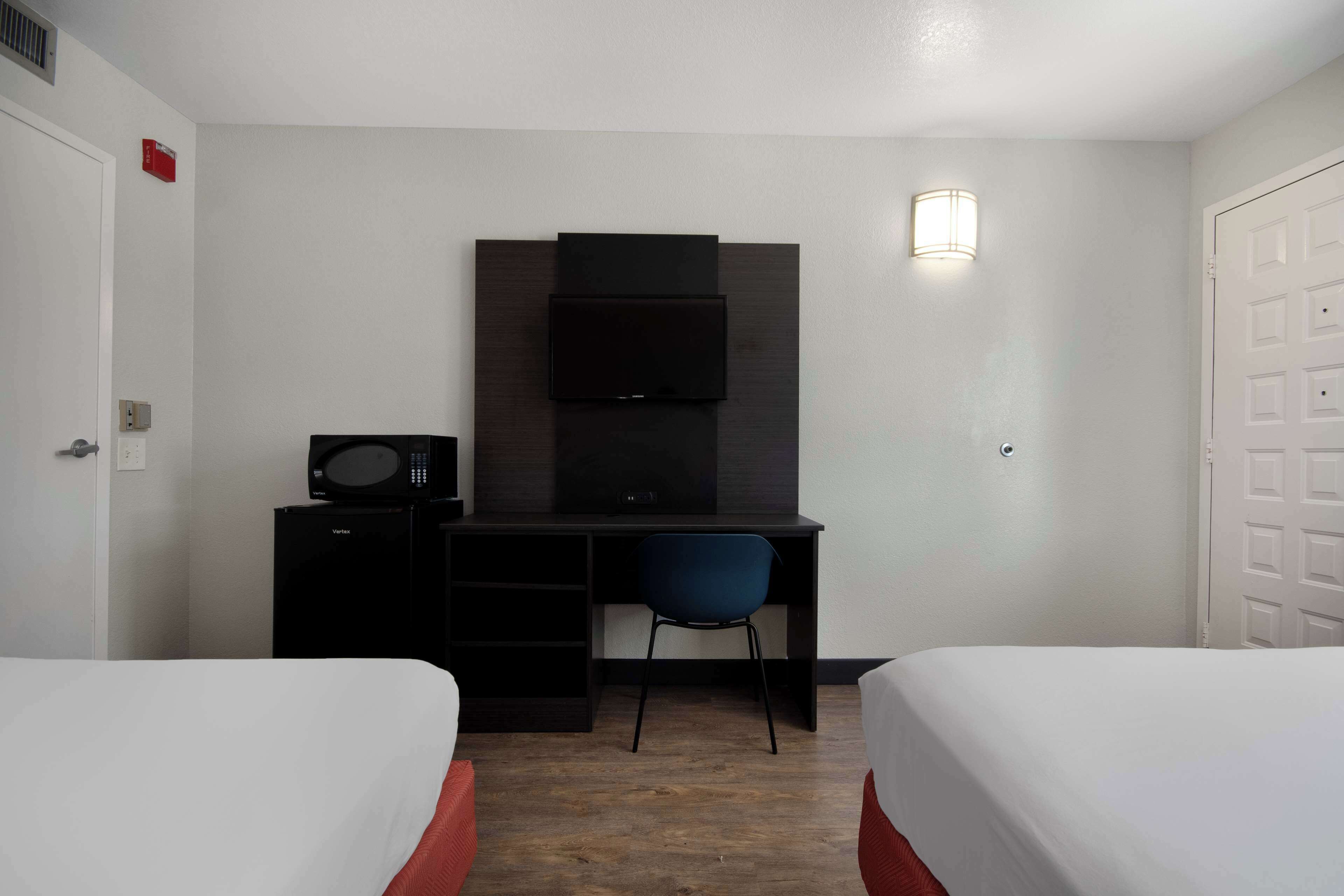 Habitación de hotel con dos camas, un escritorio con silla, microondas y televisor.