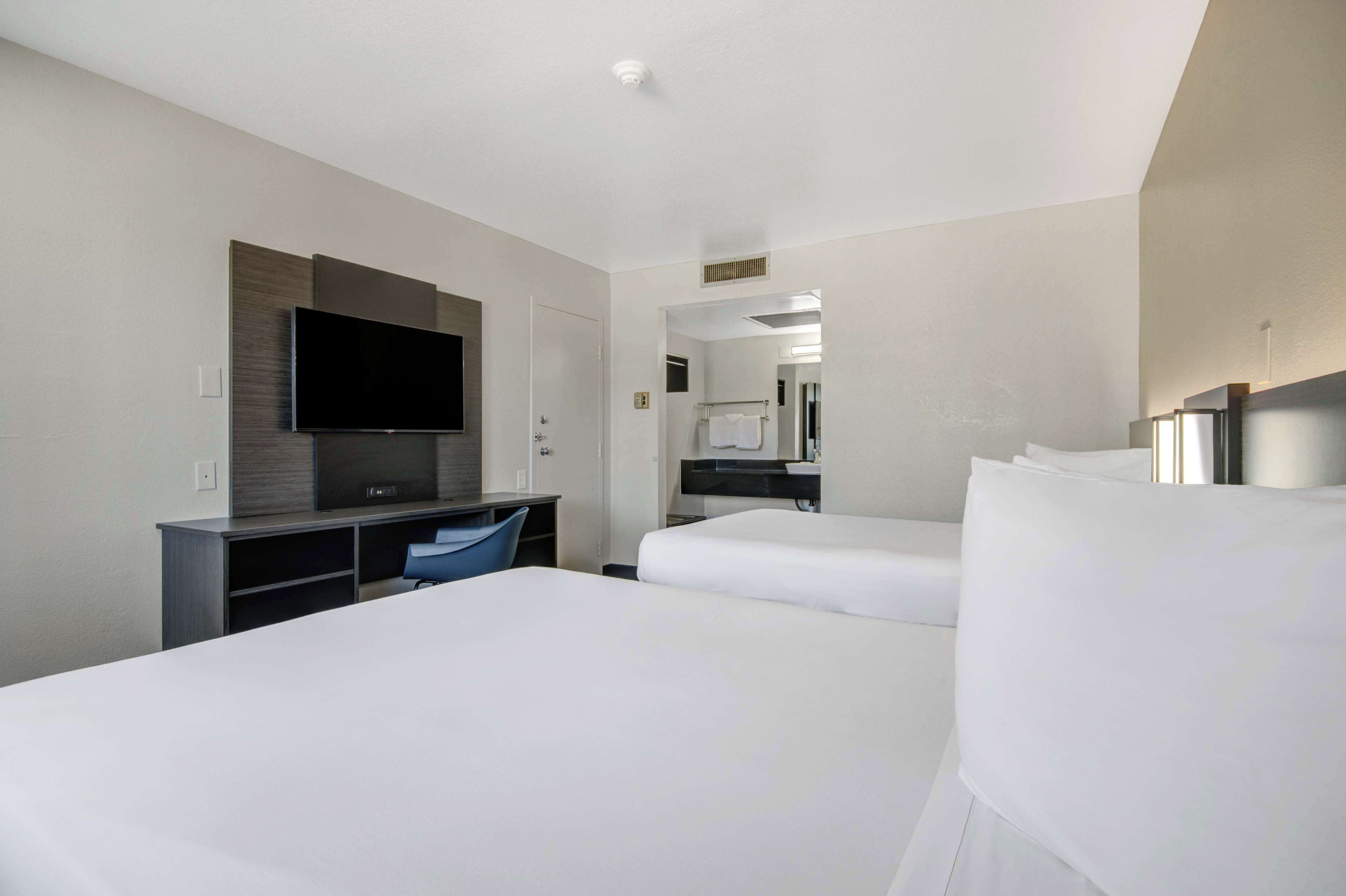 A hotel room with two beds, a flat-screen TV, a desk, and a mirror.