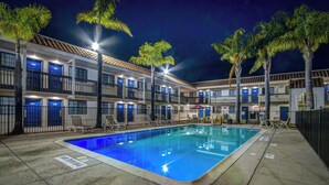 A hotel with a swimming pool, multiple balconies, and palm trees.